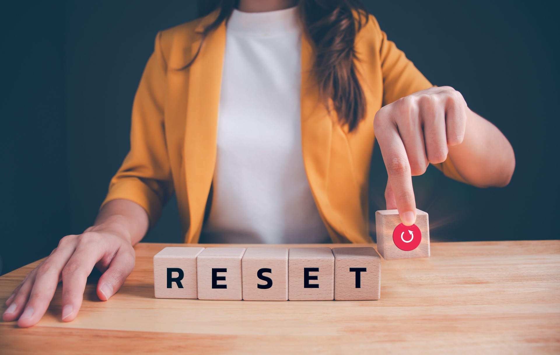Businesswoman in a yellow suit is picking up wooden blocks with words RESET and red reset icon. Concept of  make a new beginning and resetting computer, life, business or career.