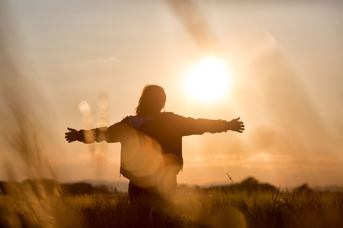Middle aged caucasian woman standing in the sunlit field with open arms, embracing nature