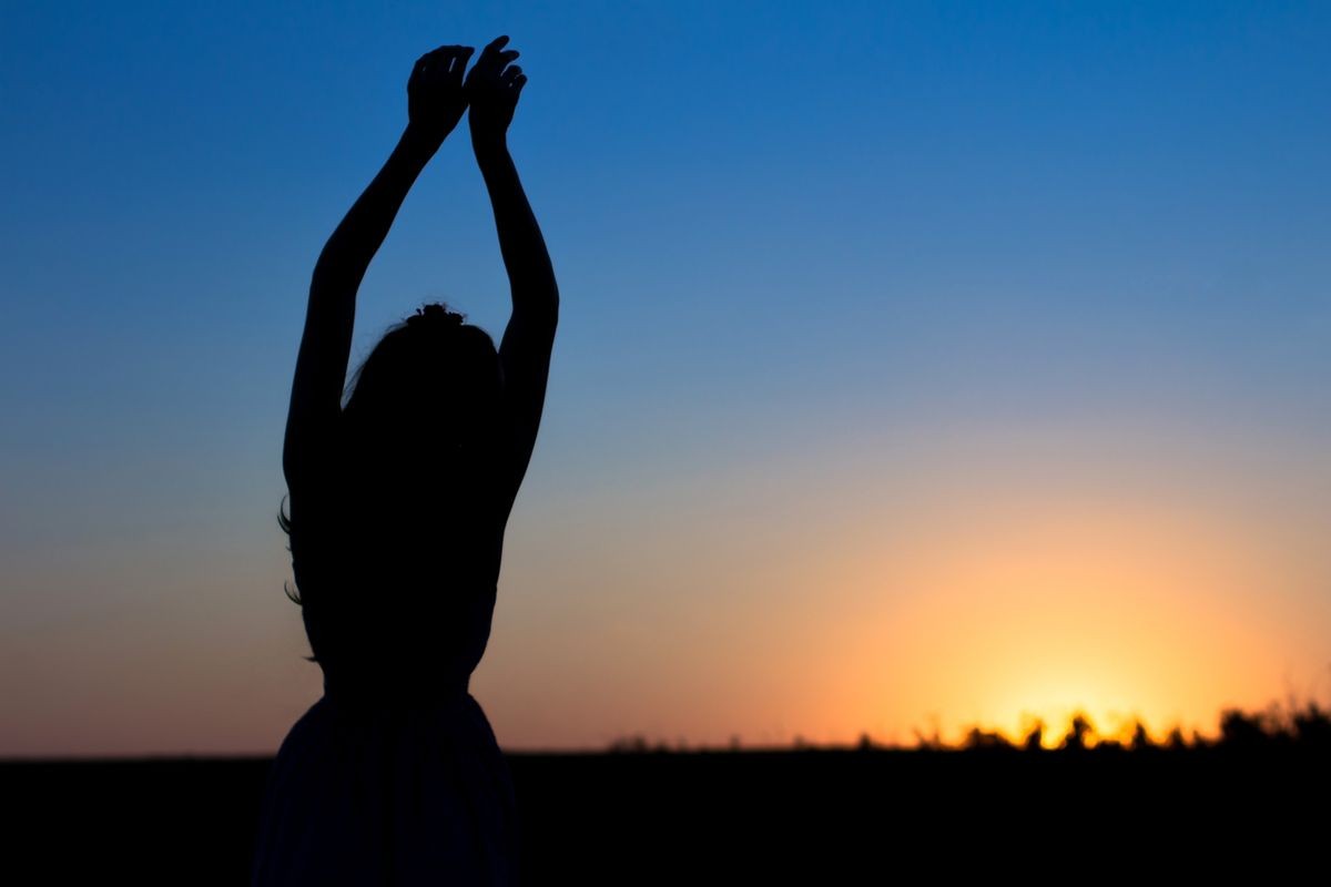 Silhouette of a woman hands up against a blue sky. Sunset or dawn.
The concept of harmony and health woman 
